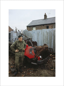 2nd Lieutenant Jonathan Clarke, 1st Royal Green Jackets, with the wreckage of a burnt out car in Belfast, December 1969.