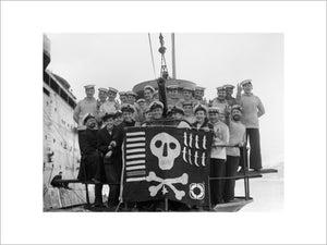 The crew of HM Submarine UTMOST displaying their "Jolly Roger" at Holy Loch in Scotland after a successful year's service in the Mediterranean, 6 February 1942.