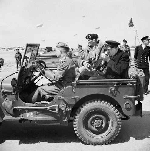 Winston Churchill lights a cigar in the back of a jeep while touring the Normandy beaches with General Mongomery, 12 June 1944.