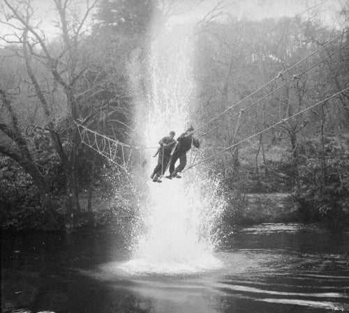 Commandos cross a river on a 'toggle bridge' under simulated artillery fire at the Commando training depot at Achnacarry in Scotland, January 1943.