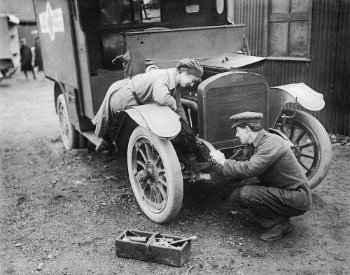 An ambulance driver of the First Aid Nursing Yeomanry (FANY) assists with the maintenance of her vehicle at St Omer, 28 February 1917.