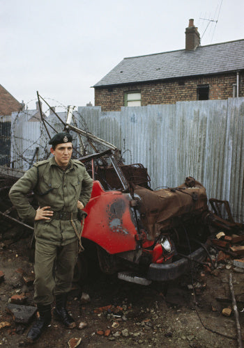 2nd Lieutenant Jonathan Clarke, 1st Royal Green Jackets, with the wreckage of a burnt out car in Belfast, December 1969.