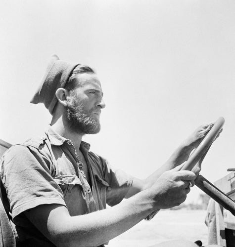 The Western Desert 1942: Head and shoulders portrait of a bearded member of the Long Range Desert Group wearing a woolly cap at the wheel of his jeep.