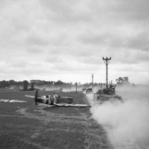 Sherman tanks move up past a crash-landed Spitfire, for an attack on Tilly-sur-Seulles, Normandy, 17 June 1944.