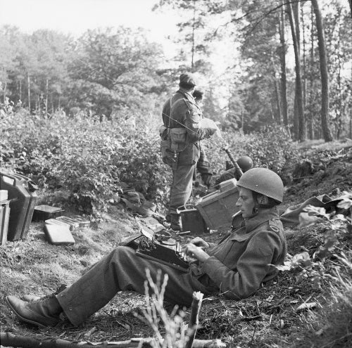 War Correspondent Alan Wood is seen typing his despatch, while Airborne troops in the background consult a map during Operation 'Market Garden', Holland, 18 September 1944.