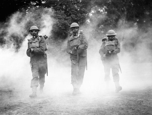 Irish Guards wearing gasmasks advance through smoke with 'tommy guns' at the ready, at Nooks Head near Woking in Surrey, 8 July 1940.
