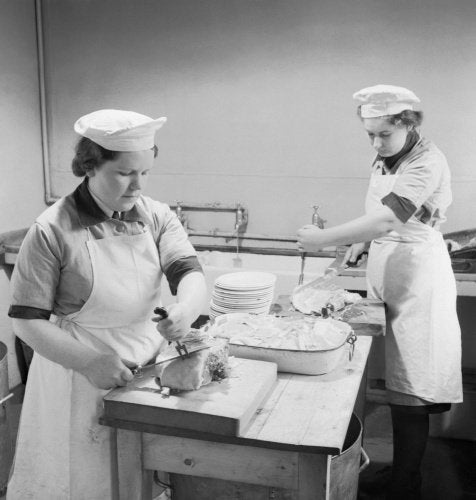Two Wren cooks carve ham for the lunchtime meal in the galley of a Fleet Air Arm base in Scotland, 1943.
