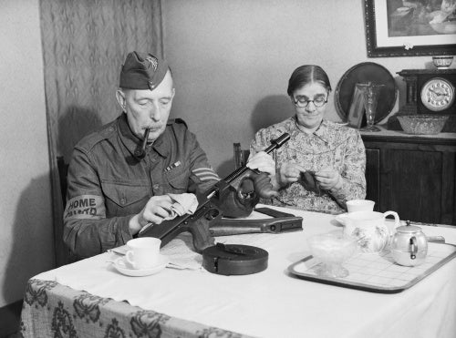 A veteran sergeant in the Dorking Home Guard cleans his Tommy gun at the dining room table, before going on parade, 1 December 1940.