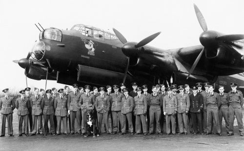Aircrew of No. 106 Squadron RAF gather in front of the Avro Lancaster flown by the Squadron CO, Wing Commander Guy Gibson (centre, to right of dog), to mark the completion of his first tour of operations, Syerston in Nottinghamshire, March 1943.
