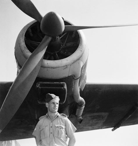 A relaxed portrait of a corporal of the Royal Air Force as he stands under the port engine of Consolidated Liberator Mark II, AL511 'A', of No. 108 Squadron RAF at Fayid, Egypt.  This aircraft is decorated with 'Dumbo' nose art.